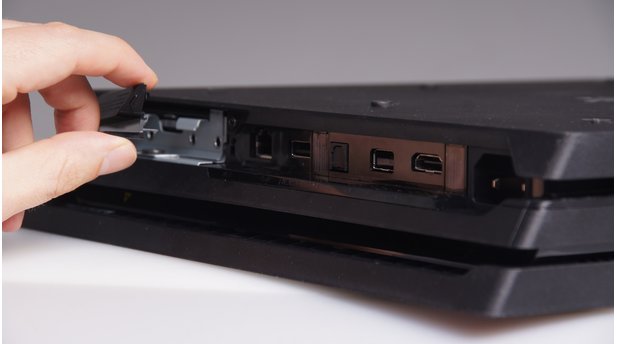 Um die Festplatte der PlayStation 4 Pro zu tauschen, müssen Sie zunächst diese Abdeckung neben den Anschlüssen auf der Rückseite durch seitlichen Druck am kleinen Pfeil-Symbol abmontieren.