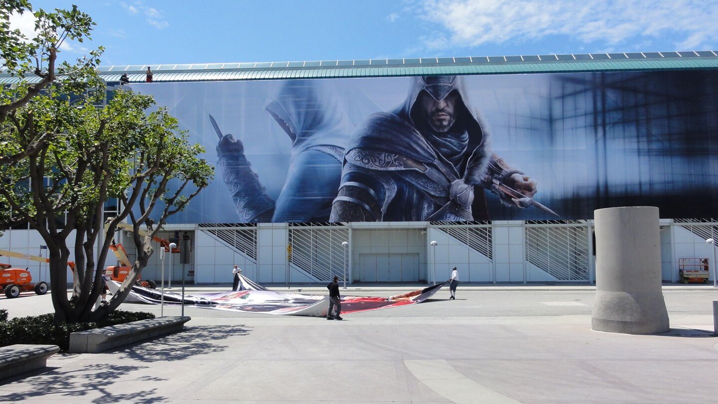 E3 2011: Schlacht um AufmerksamkeitDirekt unter den wachsamen Augen der Assassin’s Creed-Helden breiten Aufbauhelfer ein weiteres der riesigen Plakate aus – tapezieren ist einfacher.
