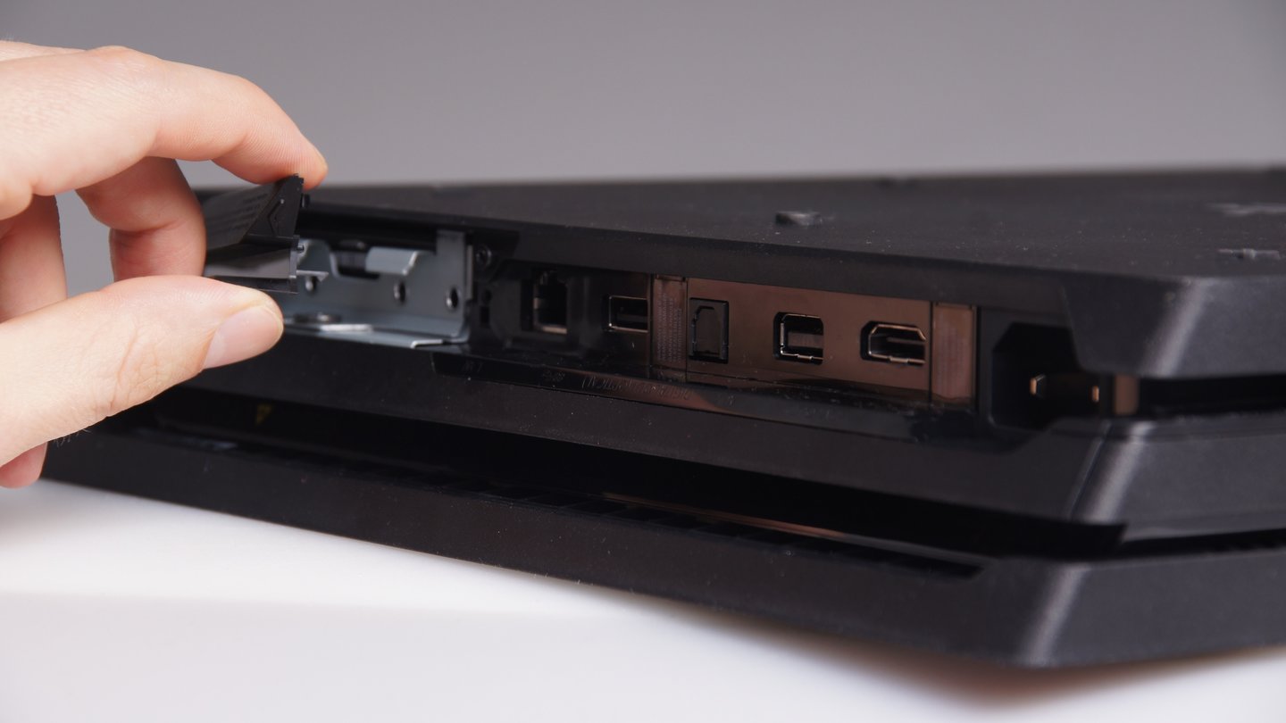 Um die Festplatte der PlayStation 4 Pro zu tauschen, müssen Sie zunächst diese Abdeckung neben den Anschlüssen auf der Rückseite durch seitlichen Druck am kleinen Pfeil-Symbol abmontieren.