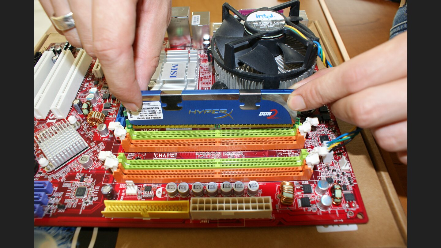 Um den Arbeitsspeicher einzubauen, klappen Sie zuerst die weißen Befestigungsnasen an den Steckplätzen nach außen. Nehmen Sie nun einen der Speicherriegel und führen Sie ihn in die seitlichen Schienen des Steckplatzes.