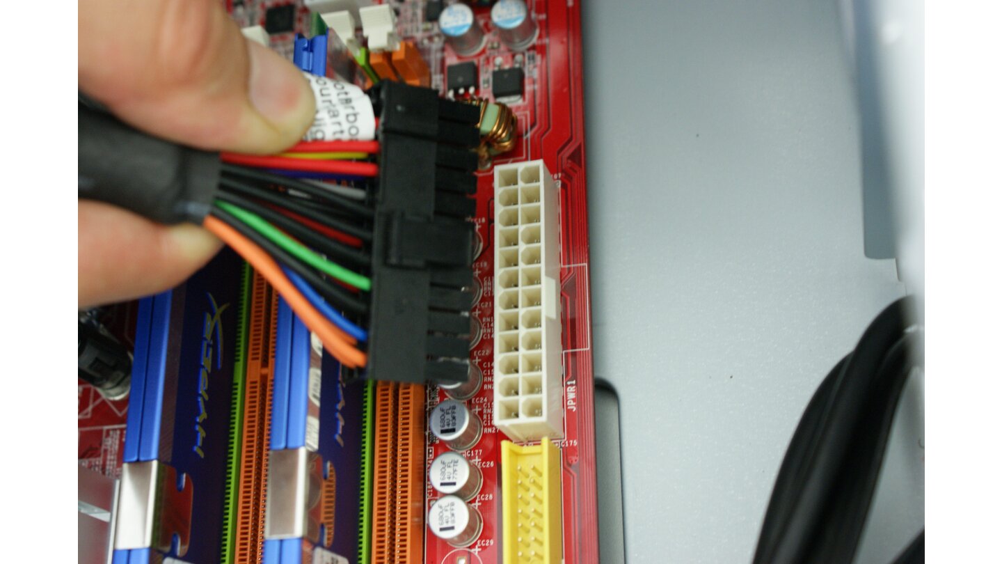 Im nächsten Schritt verbinden Sie das Mainboard mit dem Netzteil. Nehmen Sie dazu den schwarzen 24-Pol-Stecker des Netzteiles und richten Sie dessen Klammermechanismus passend zur Nase der weißen Steckleiste auf dem Mainboard aus.