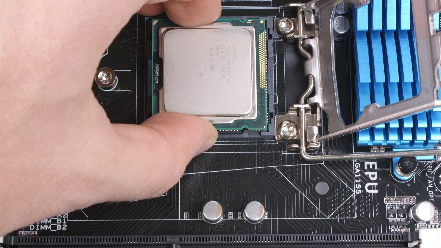 Setzt den Prozessor vorsichtig in den entriegelten Sockel. Vermeidet, die Kontakte an der Unterseite zu berühren. Am besten fasst Ihr den Prozessor seitlich an und setzt ihn von oben auf den Sockel. Die CPU passt nur in einer Richtung: Zwei Kerben an den Seiten der CPU, die exakt auf die Plastiknasen im Sockel passen, geben die Richtung vor.