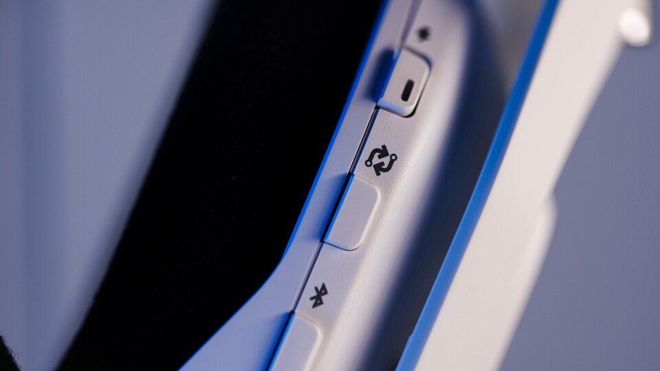 Ihr seht die rechte Ohrmuschel des weißen Astro A50 X. Der Wechsel von Gerät zu Gerät ist gemütlich von der Couch aus machbar. Dazu drückt ihr nur den Knopf mit den zwei Pfeilen. (Bild: Logitech)