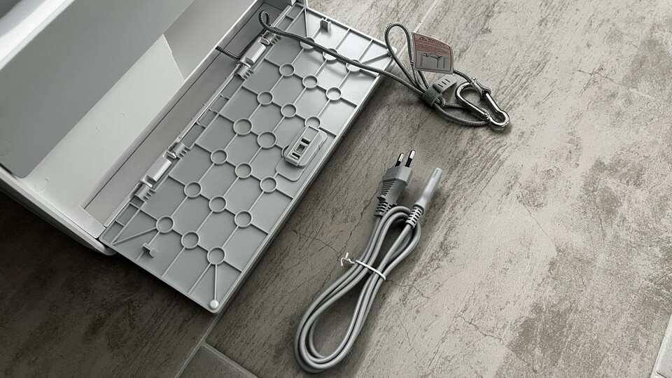 In der Rückseite finden die optionale Sicherungsleine, das Stromkabel sowie ein zweites Putztuch Platz.