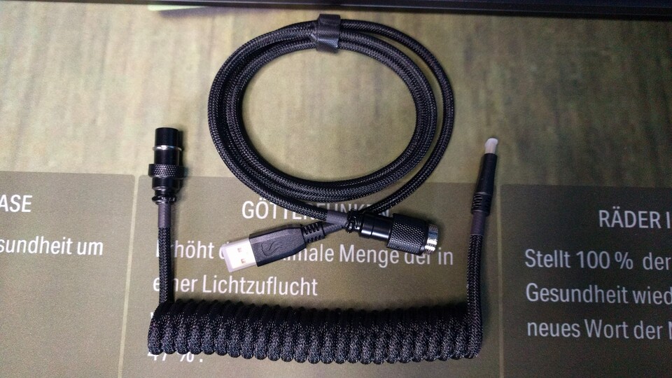 Hier zu sehen ist das Coiled-Cable, bestehend aus zwei Teilen, die zusammengeschraubt werden. Wer es weniger wuchtig mag, kann aber auch eine ganz gewöhnliche Schnur bekommen.