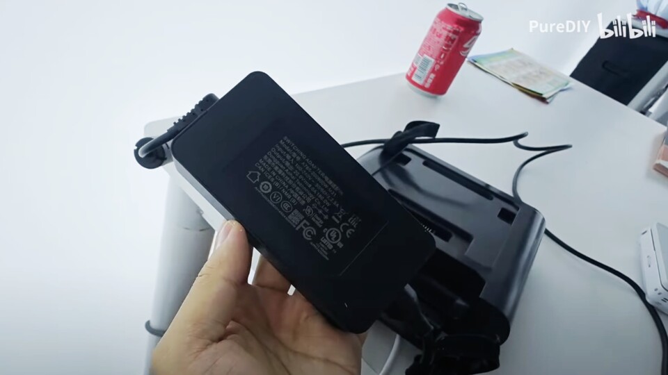 Das Netzteil ähnelt denen von Laptops. Im Hintergrund seht ihr außerdem die Docking-Station. (Bildquelle: GPD Game ConsoleYouTube)