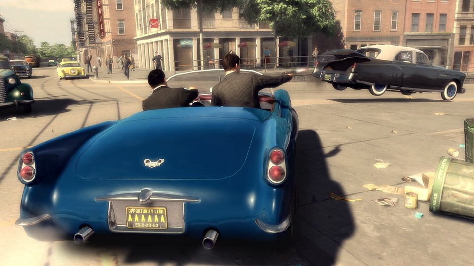 Während Joe das 40er-Jahre-Cabrio durch Empire City steuert, feuert Vito vom Beifahrersitz aus auf das flüchtende Fahrzeug, das bereits Schäden davongetragen hat.