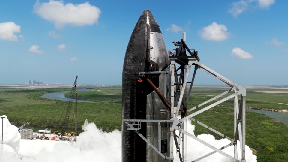 Das neue Starship, genauer die Oberstufe, auf der Masseys Testanlage. Sie befindet sich unweit der Starbase im Landesinneren. Im Hintergrund könnt ihr die inzwischen weltweit bekannte Startbasis für alle Starships erkennen.
(Bildquelle: SpaceX)